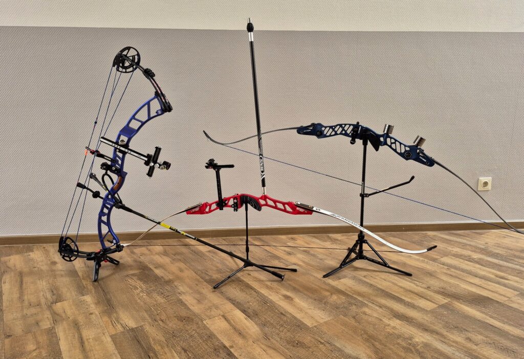 Drei Bögen nebeneinander: Compoundbogen, olympischer Recurve mit Visier und Stabilisatoren sowie Blankbogen-Recurve auf einem Ständer